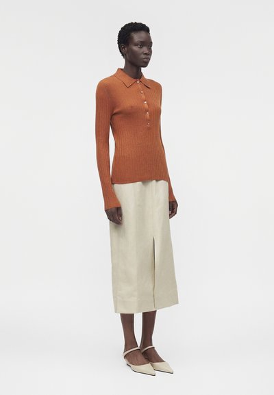 Γυναίκα που φορεί ριγωτό πόλο πουλόβερ μακρυμάνικο σε σκουριά χρώμα, μπεζ midi φούστα με σκίσιμο μπροστά και μπεζ slingback παπούτσια με μυτερό μπροστινό μέρος.