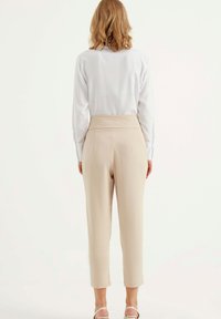 Beige hoge taille broek met een gladde textuur, taps toelopende benen en subtiele naden, gecombineerd met een witte blouse met lange mouwen.