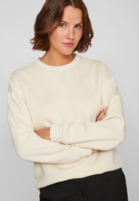 Crème kleurige sweatshirt met een ronde hals, lange mouwen en geribbelde manchetten. Zachte textuur met een ontspannen pasvorm; geen patronen of accenten zichtbaar.