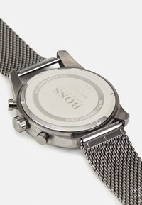 Montre en acier inoxydable avec un bracelet en maille métallique. Boîtier rond avec couronne et poussoirs, fond de boîtier gravé, étanche jusqu'à 5 bars.