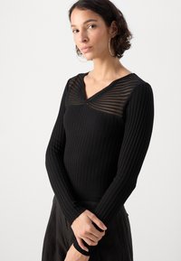 Svart ribbestrikket langermet topp med en gjennomsiktig stripete utringning, slim fit og strukturet stoff. Designet har en V-formet krage.