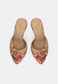 Tacones slingback florales en beige suave con patrones de rosas rosas. Diseño de punta puntiaguda con un detalle de nudo en la parte delantera. Textura suave.
