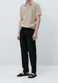 Beige neulepikeepaita, jossa on lyhyt kaulus, yhdistettynä mustiin housuihin ja mustiin sandaaleihin, mattapintainen ja suora leikkaus.