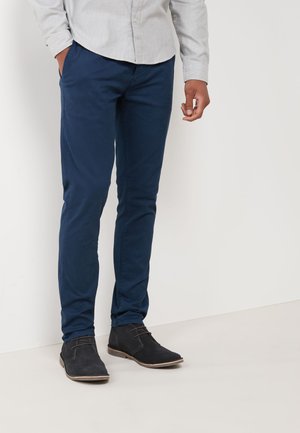 Navy blue chinos made from a soft fabric, featuring a slim fit. Paired with black suede ankle boots with stitching accents.