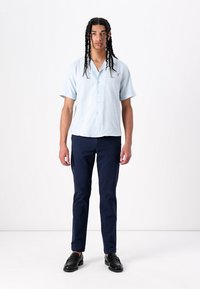 Chemise bleu clair à manches courtes, boutonnée, en tissu léger, associée à un pantalon ajusté bleu marine et à des mocassins noirs.