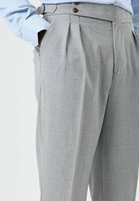 Pantalon plissé gris clair en tissu texturé, avec deux poches avant et deux boutons à la taille.