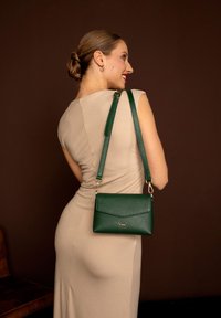 Zelená kožená crossbody taška s textura povrchu, elegantním designem, zlatými kovovými doplňky a nastavitelním popruhem.