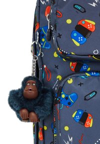 Der Rucksack besteht aus einem dunkelgrauen Stoff mit bunten Mustern von Gaming-Controllern. Ein angenähtes Plüsch-Schlüsselanhänger zeigt einen braunhäutigen Affen mit blauen Fellen.
