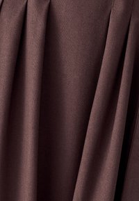 Tmavě hnědá látka se jemnými záhyby a viditelnou tkanou strukturou, visící svisle v jemných záhybech.