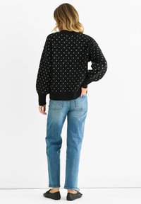Black knitted sweater with white polka dots, long sleeves, and ribbed hem. Paired with light blue straight-leg jeans and black shoes.