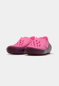 Pár ružových slip-on topánok s perforovaným zvrškom a текстúrovanou tmavou podrážkou, naklonených mierne doprava na bielom pozadí.