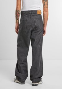 Svarte denim vidbenede bukser med høj talje, synlige sømme, to baglommer og et brunt lædermærke på taljebåndet.
