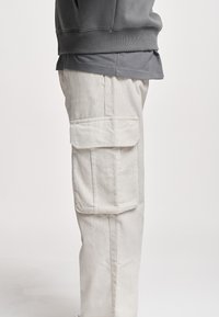 Hvite cordbukser med sidelommer, synlig vertikal ribbe tekstur, og rett ben design. Brukt med en grå hettegenser.