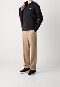 Czarny t-shirt z krótkim rękawem z logo, nałożony na bluzkę z długim rękawem; beżowe spodnie; czarne sneakersy. Minimalistyczny styl, gładka tekstura.