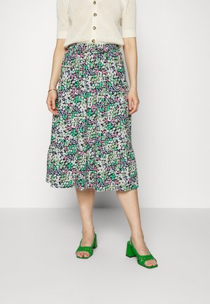 Saia midi floral com padrões em verde, rosa e branco sobre um fundo escuro. Tecido texturizado com cintura elástica. Combinada com sandálias de salto verde.
