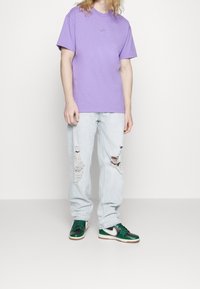 Paars T-shirt met ronde hals, lichtgewassen jeans met slijtageplekken en groene/zwartkleurige sneakers met witte accenten. Casual, ontspannen pasvorm.