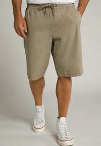 Shorts beige arrivant aux genoux avec une taille élastique et un cordon de serrage. Comprend des poches latérales et un tissu lisse et léger. Portés avec des baskets blanches.