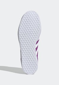 Semelle de chaussure en caoutchouc blanc, présentant un motif de grip texturé. Le côté est violet avec des rayures blanches. Design athlétique standard, forme plate.