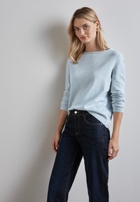 Maglione blu chiaro in morbido tessuto con scollo rotondo e polsini a costine, abbinato a jeans di denim scuro con dettagli di cuciture.