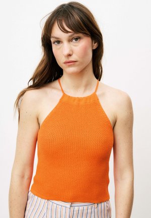 Orange gestricktes Oberteil mit halter-neck und strukturiertem Muster, das einen hohen Ausschnitt und dünne Träger besitzt. Kombiniert mit gestreiften Hosen.