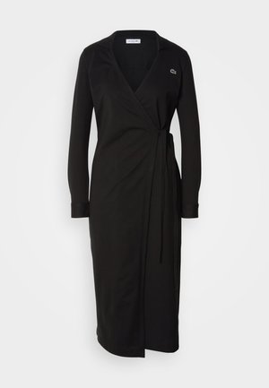 Schwarzes Wickelkleid aus weichem Stoff, mit langen Ärmeln, einem Kragen und einem seitlichen Bindegürtel; beinhaltet ein kleines grünes Logo auf der Brust.
