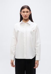 Λευκό βαμβακερό πουκάμισο με κουμπιά, διαθέτει τσέπη στο στήθος και μικρό λογότυπο. Μακριά μανίκια με μανσέτες που κουμπώνουν, άνετη εφαρμογή. Λεπτή υφή.