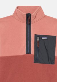 Pullover di pile corallo e blu scuro con colletto a mezza zip, dotato di tasca sul petto con zip e etichetta del marchio.