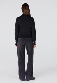 Zwarte gebreide trui met lange mouwen, aansluitende tailleband, gecombineerd met hoog-nagedragen donkere denim wijde broek met zijzakken en naden.