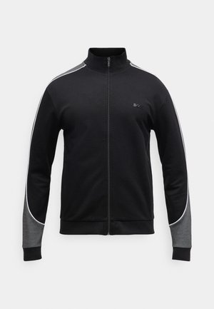 Černá sportovní bunda s vysokým límcem, předním zipem, šedými akcenty na rukávech a bílým lemem podél ramen. Jemná textura látky.