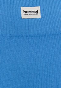 Blauer Rippstoff mit weißem rechteckigem Etikett mit der Aufschrift "hummel PERFORMANCE", nahe der oberen Mitte angenäht.