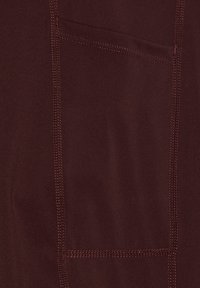 Burgundy tyg med en slät textur, med kontrasterande sömmar och en lapplomme på vänster sida.