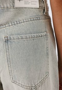 Jeans de denim azul claro con un bolsillo trasero con costuras visibles, una etiqueta blanca en la cintura y una superficie texturizada y acanalada.