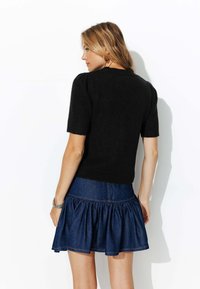 Pull noir à manches courtes en tissu texturé, associé à une jupe en denim avec un ourlet volanté et une couleur indigo foncé.