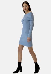 Rippstrickkleid in Hellblau, mit schulterfreiem Design, langen Ärmeln und figurbetonender Silhouette. Schwarze Knöchelstiefel.