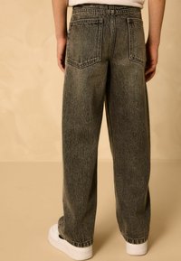 Sötét szürke denim széles lábú farmer, két hátsó zsebbel és nyers szegéllyel. Fehér sportcipővel párosítva, hogy laza megjelenést nyújtson.