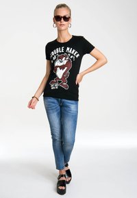Black t-shirt with "Double Maker" text and a cartoon Tasmanian Devil graphic. Paired with blue jeans and black platform sandals.
