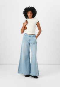 Lyseblå vide jeans laget av denim, med høy midje og rett snitt; kombinert med en tettsittende kremfarget topp og svarte sko.