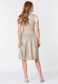 Beiges Kleid mit aufwendigen Mustern, figurbetontem Oberteil, plissiertem Rock und einem Satin-Gürtel. Ergänzt durch leichte Spitzenärmel und weiche Schuhe.