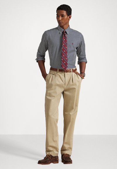 Ριγέ πουκάμισο με γυρισμένα μανίκια, μπορντώ γραβάτα με σχέδια, μπεζ παντελόνι, καφέ παπούτσια και πλεκτή ζώνη από δέρμα.