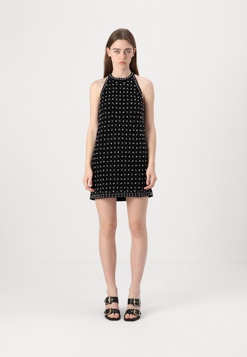 Abito halter in velluto nero con un motivo a diamante, decorato con borchie argentate lungo l'orlo. Abbinato a sandali neri con cinturini.