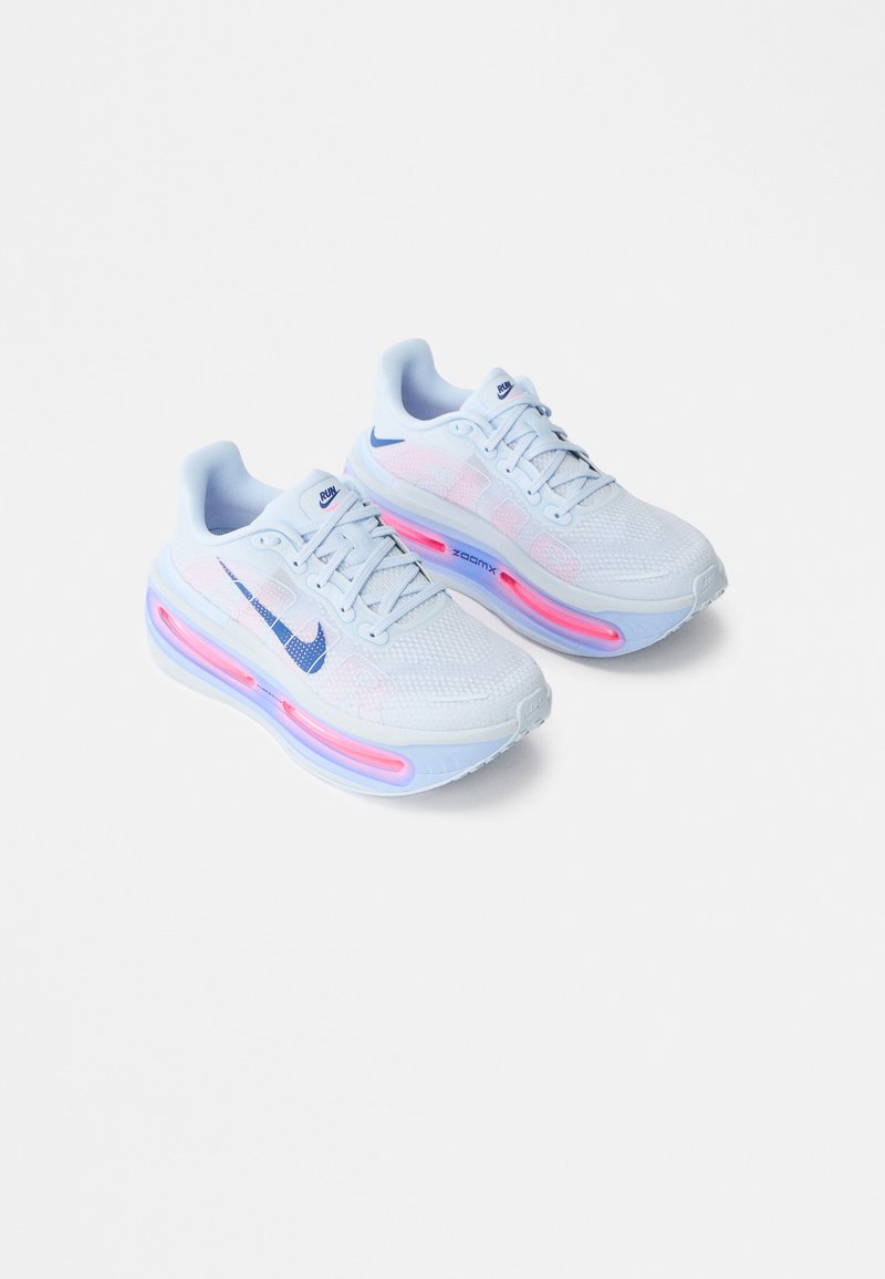 Baltos sportinės kedai su tekstūruotu tinklelio viršumi, šviesiai mėlynomis detalėmis ir matomu rausvu oro padu. Yra mėlynas Nike logotipas.