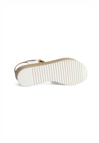 Espadrille en paille tissée avec une semelle en caoutchouc blanche, présentant un dessous texturé et une petite sangle de cheville maintenue par une boucle dorée.