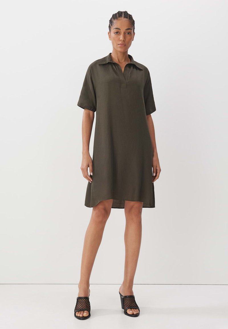 Khakifarbenes Hemdkleid mit kurzen Ärmeln, Kragen, Frontknopfleiste, Länge bis zur Mitte des Oberschenkels und glatter Textur. Getragen mit schwarzen Sandalen mit Netz-Absatz.