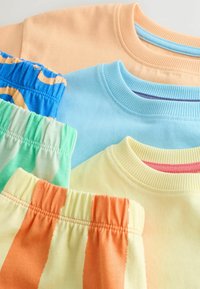 Quatre t-shirts à col rond pliés en pêche, bleu clair, jaune pâle et un motif rayé jaune-orange, associés à des ceintures élastiques assorties.