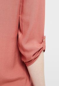 Rostfarbiges, leichtes Hemd mit hochgerollten Dreiviertelärmeln, das über einen Knopfdetails am Bündchen und eine glatte Textur verfügt.