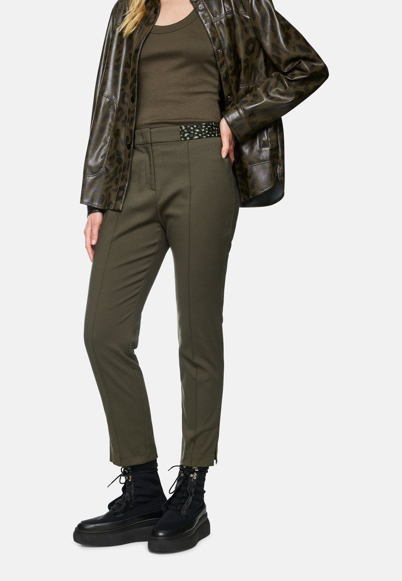 Olive green tailored pants with a smooth texture, featuring a decorative waistband and slim fit. Paired with black lace-up boots.