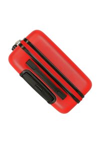 Maleta rígida roja con asa y cremallera negras, mostrada cerrada y inclinada sobre fondo blanco.