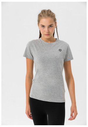 Grå kortærmet t-shirt i et blødt materiale, med et lille sort logo på venstre brystområde, parret med sorte leggings.