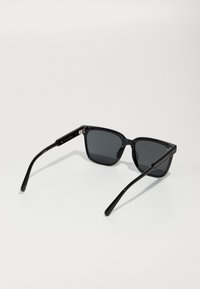 Black rectangular sunglasses with dark lenses, lightweight plastic frame, and sleek arms featuring a textured grip on the temple ends.