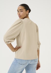 Beige puff-sleeve top made of textured fabric, featuring a rounded neckline and elasticized cuffs, paired with light blue jeans.